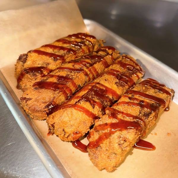 Four crispy fried seafood rolls drizzled with a sweet and tangy sauce on parchment paper.
