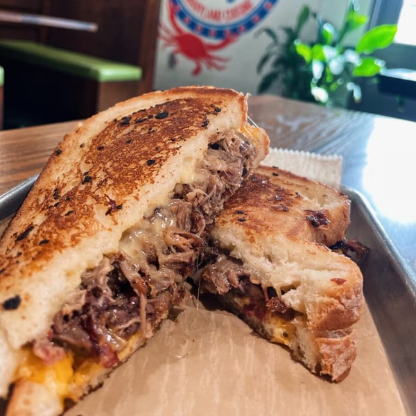 A grilled cheese sandwich filled with shredded meat and melted cheese, cut in half on a tray.