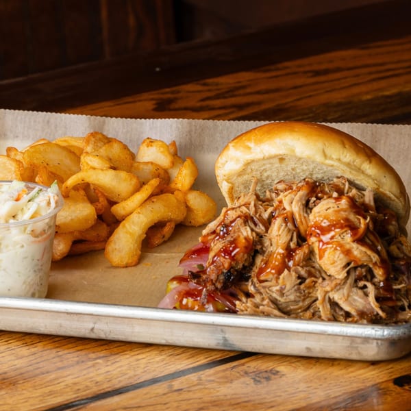Pulled pork sandwich with BBQ sauce and pickled onions, served with potato wedges and coleslaw.