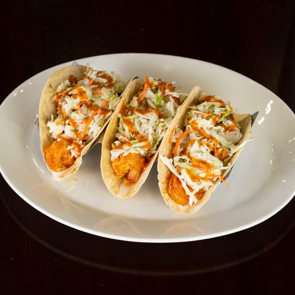 Three shrimp tacos with coleslaw and orange sauce on a white plate from Charm City Seafood.