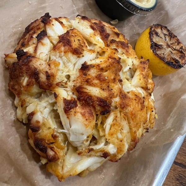 Charm City Seafood's crab cake, golden brown and flaky, served with a charred lemon and dipping sauce.